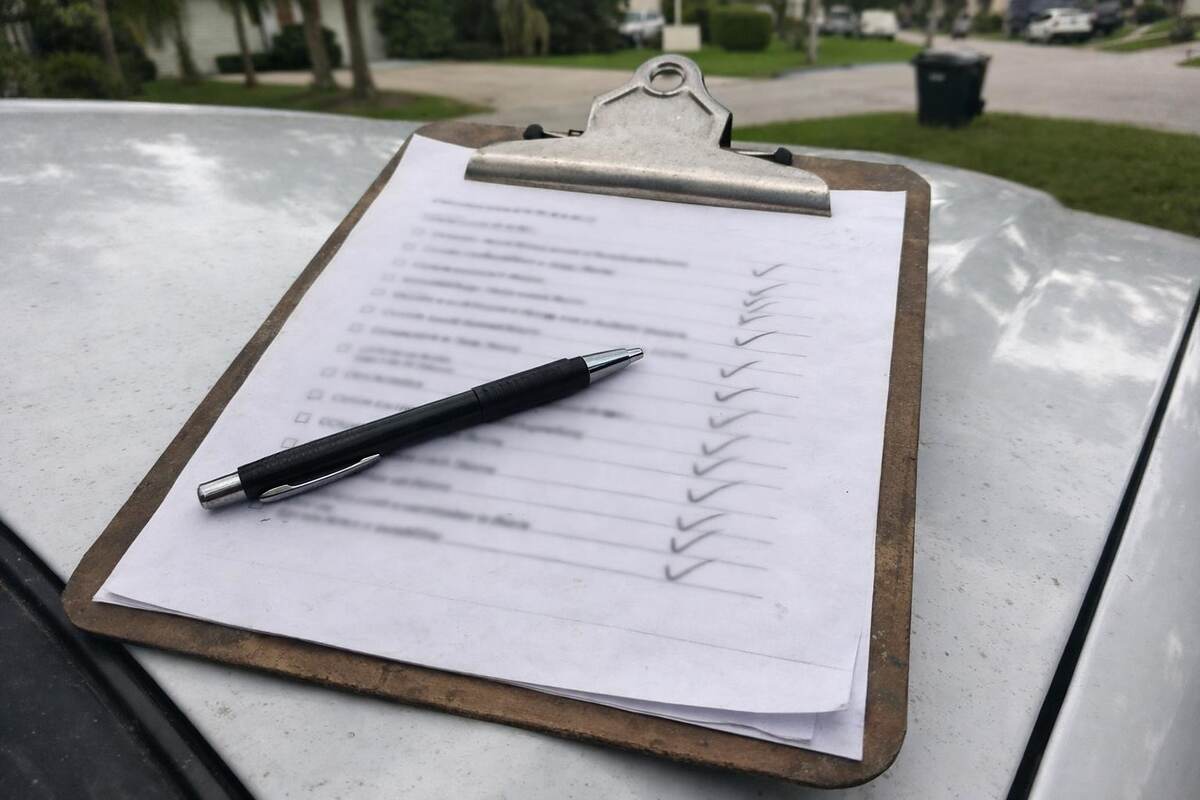 A clipboard holding a printed inspection checklist on the hood of a pickup in a driveway