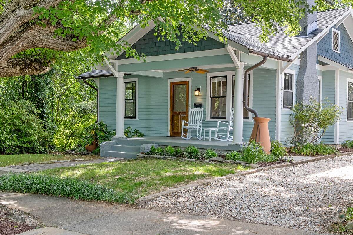 A wood-frame bungalow with a front porch under old trees