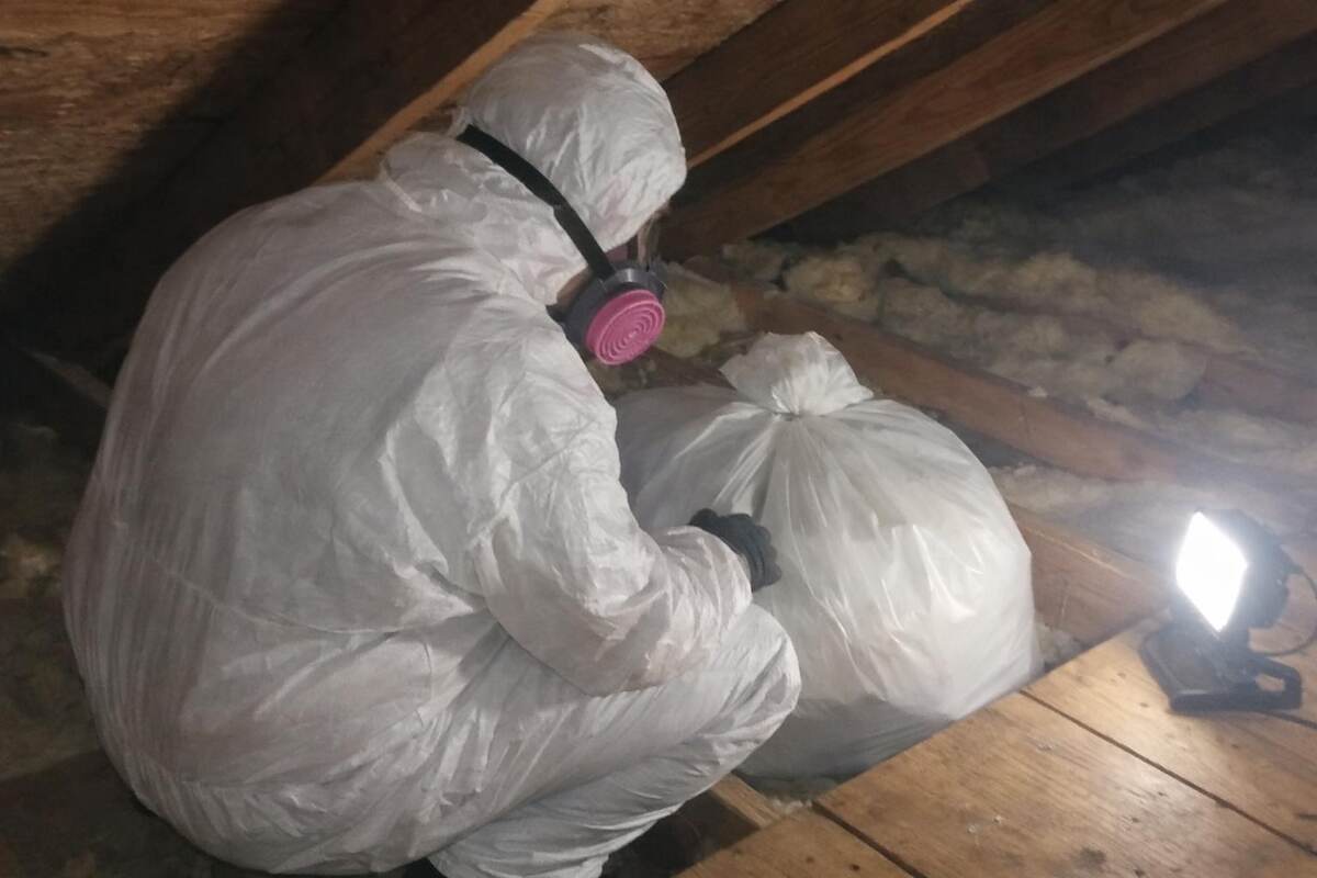A worker in a white protective suit and respirator, face turned away
